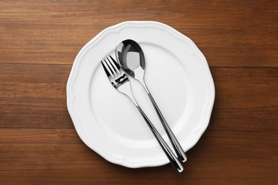 Clean plate, spoon and fork on wooden table, top view