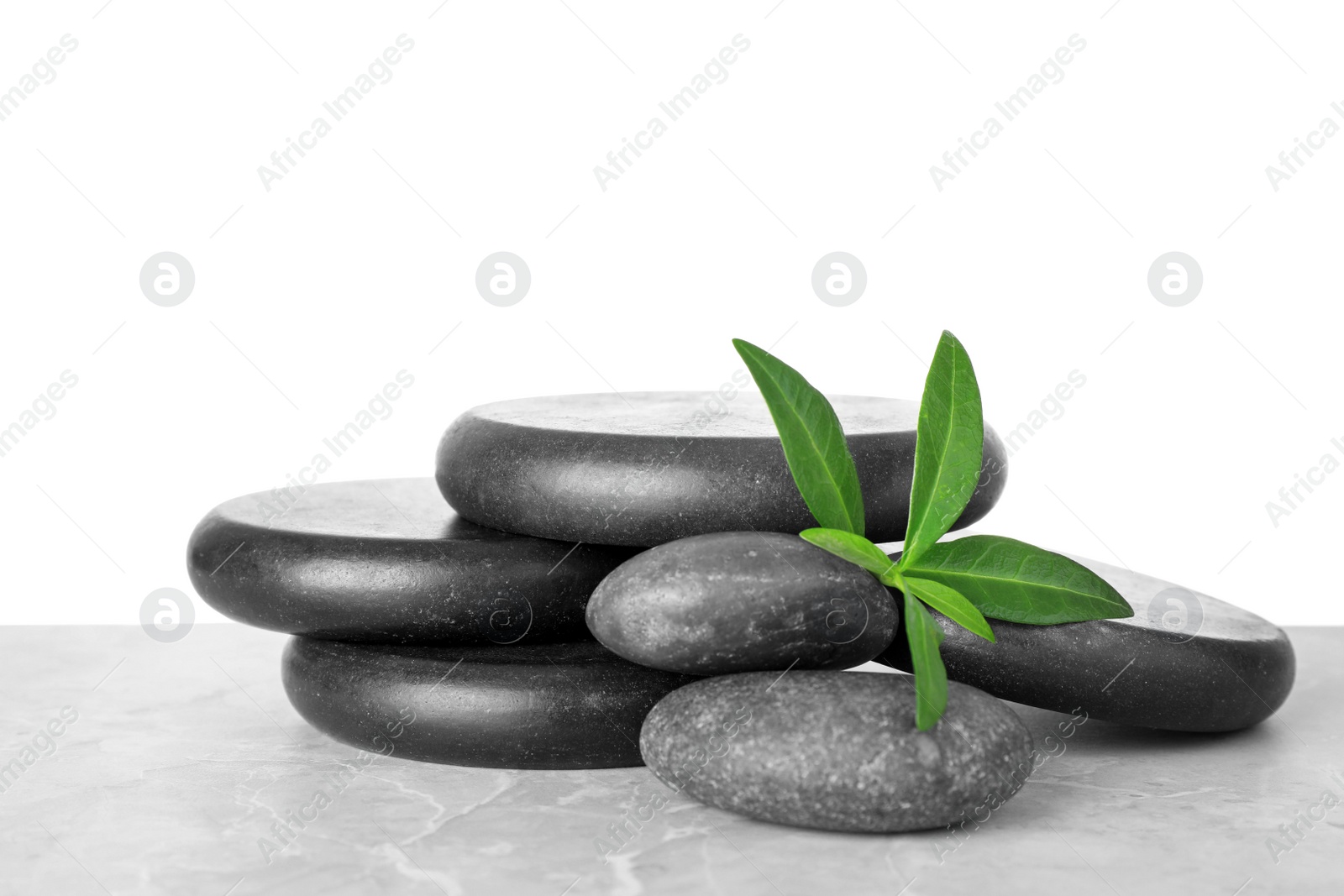 Photo of Pile of spa stones and green leaves on table against white background