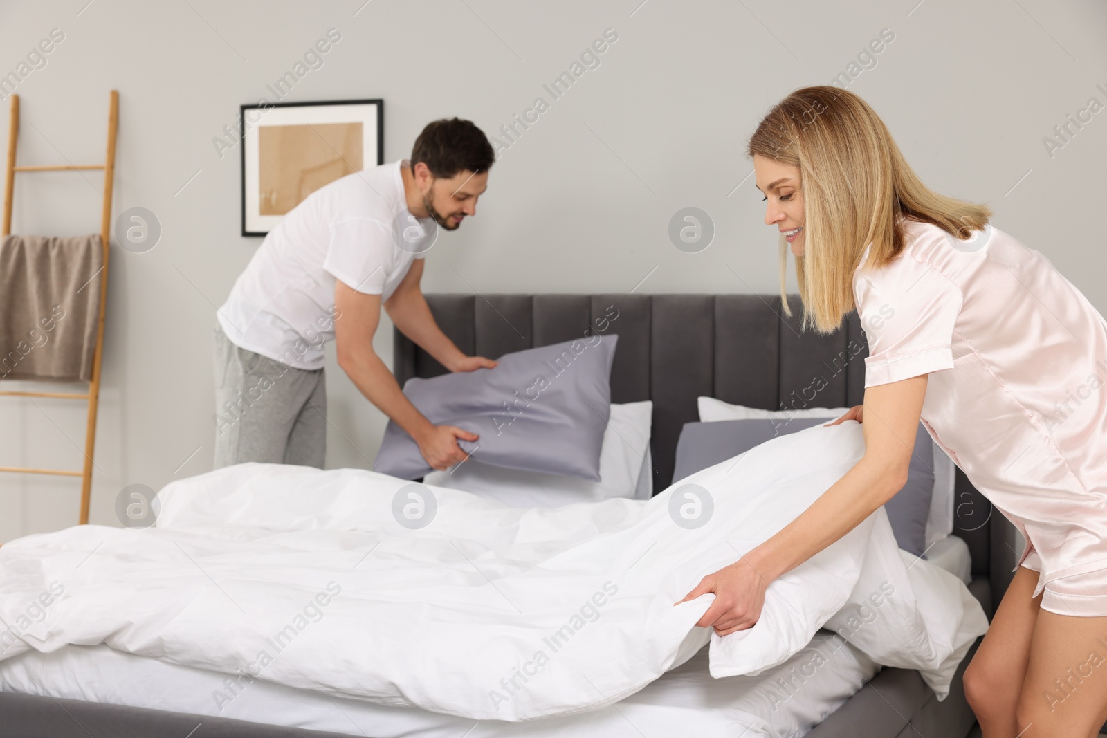 Photo of Couple changing bed linens in room. Domestic chores