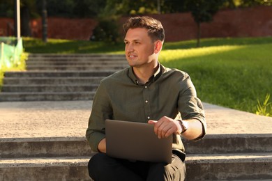 Photo of Handsome man with laptop sitting on concrete stairs outdoors