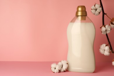 Photo of Bottle of fabric softener and fluffy cotton flowers on pink background, space for text