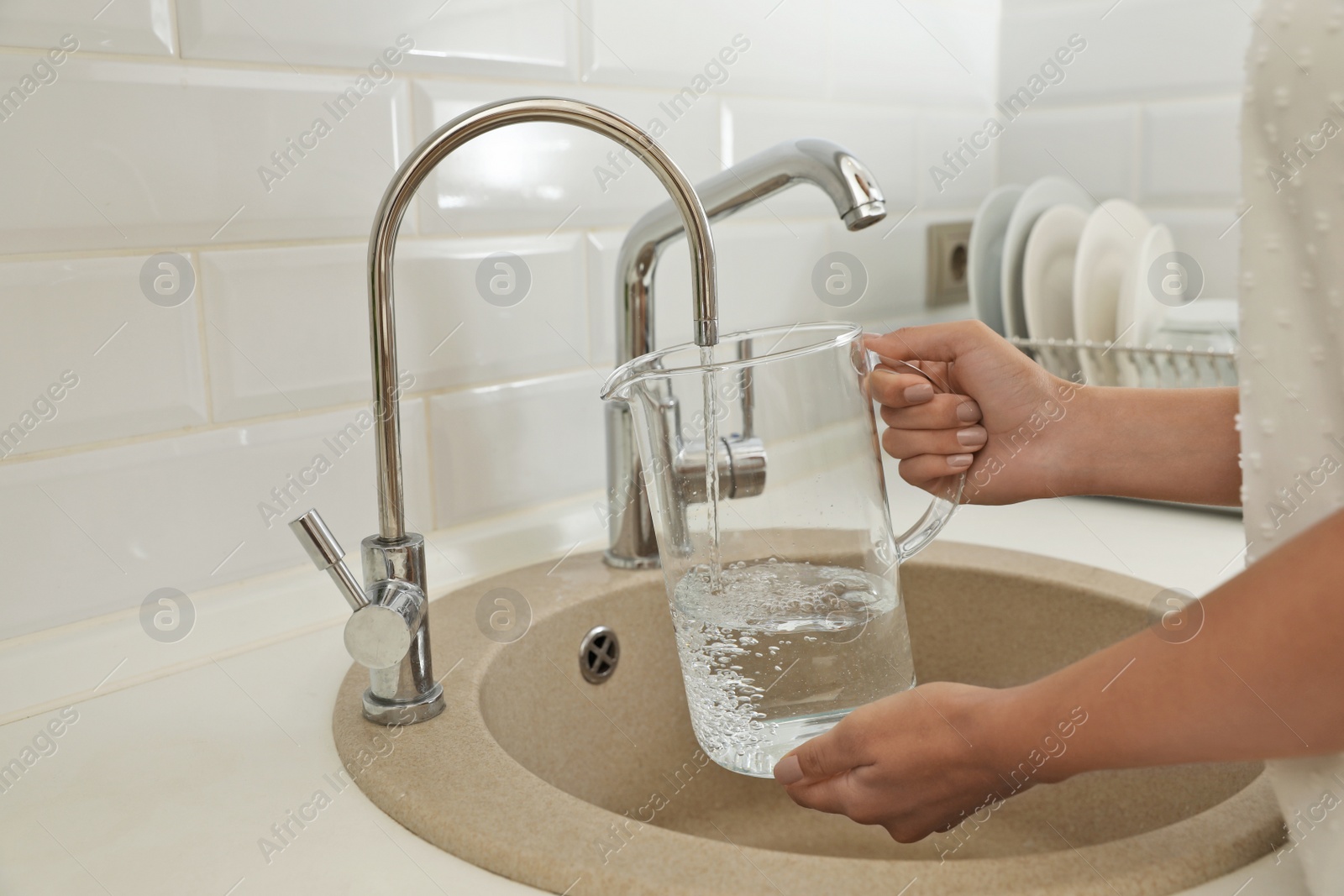 Photo of Woman pouring water into glass jug in kitchen, closeup