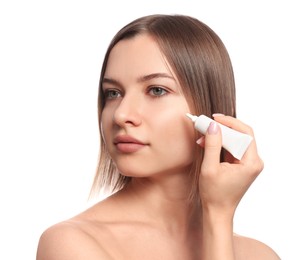 Young woman applying cream under eyes on white background