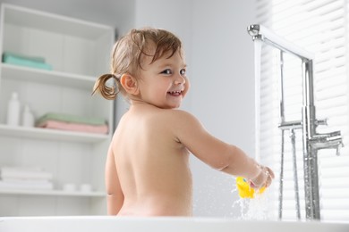 Photo of Cute little girl washing toy under faucet in bathtub at home