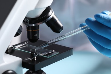 Doctor dripping liquid from pipette onto glass slide on microscope, closeup. Laboratory analysis