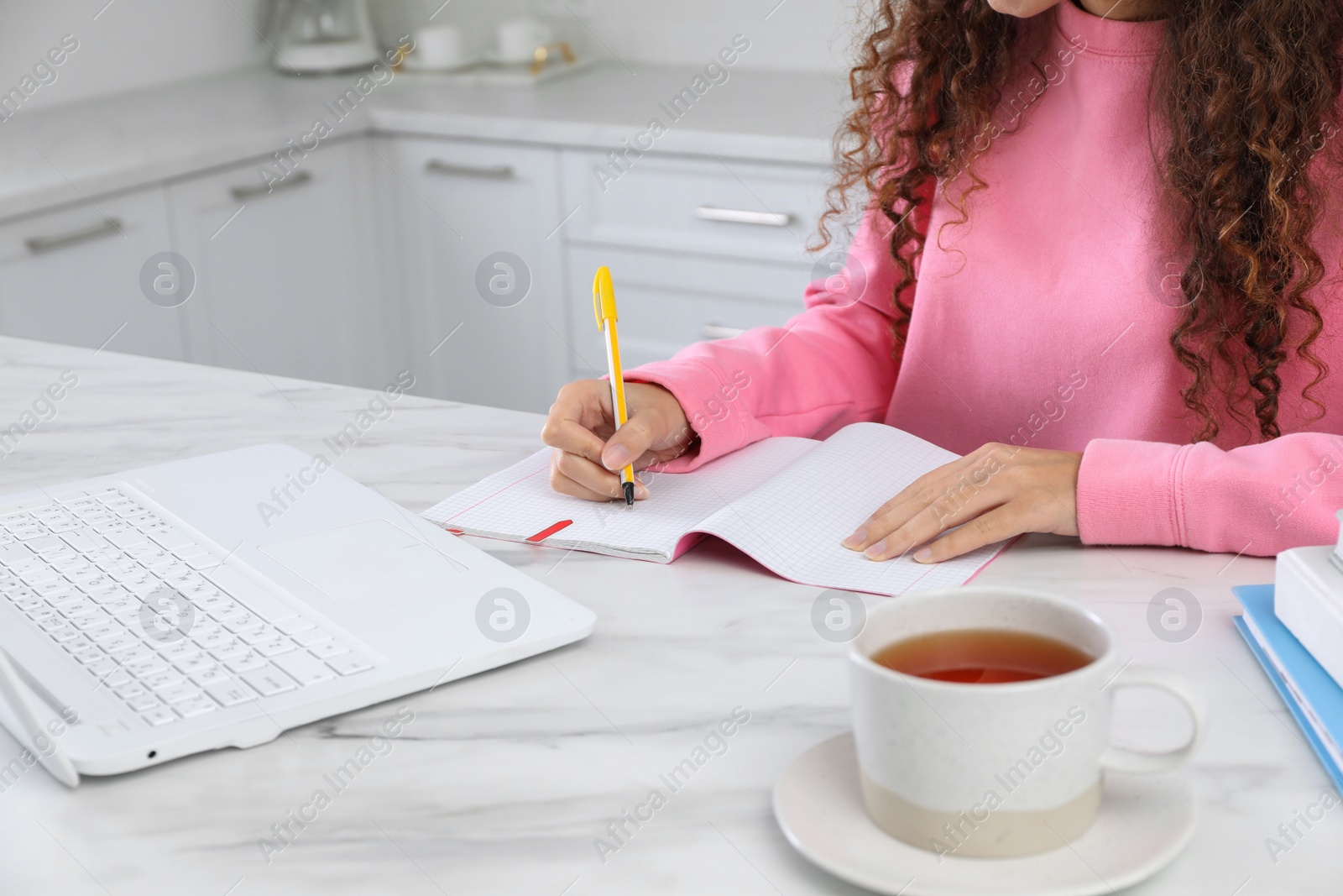 Photo of African American woman with modern laptop studying in kitchen, closeup. Distance learning