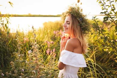 Photo of Young woman wearing wreath made of beautiful flowers outdoors on sunny day