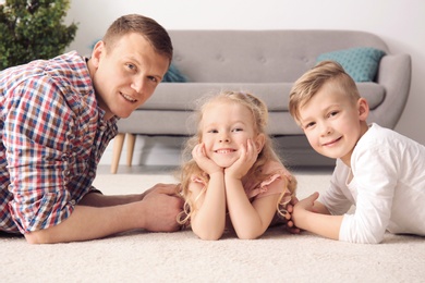 Cute little children and their father lying on cozy carpet at home