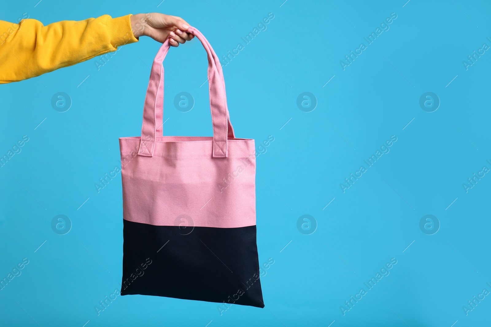 Photo of Young woman holding textile bag on blue background, closeup. Space for text