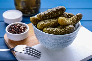 Photo of Bowl of pickled cucumbers and ingredients on blue wooden table, closeup