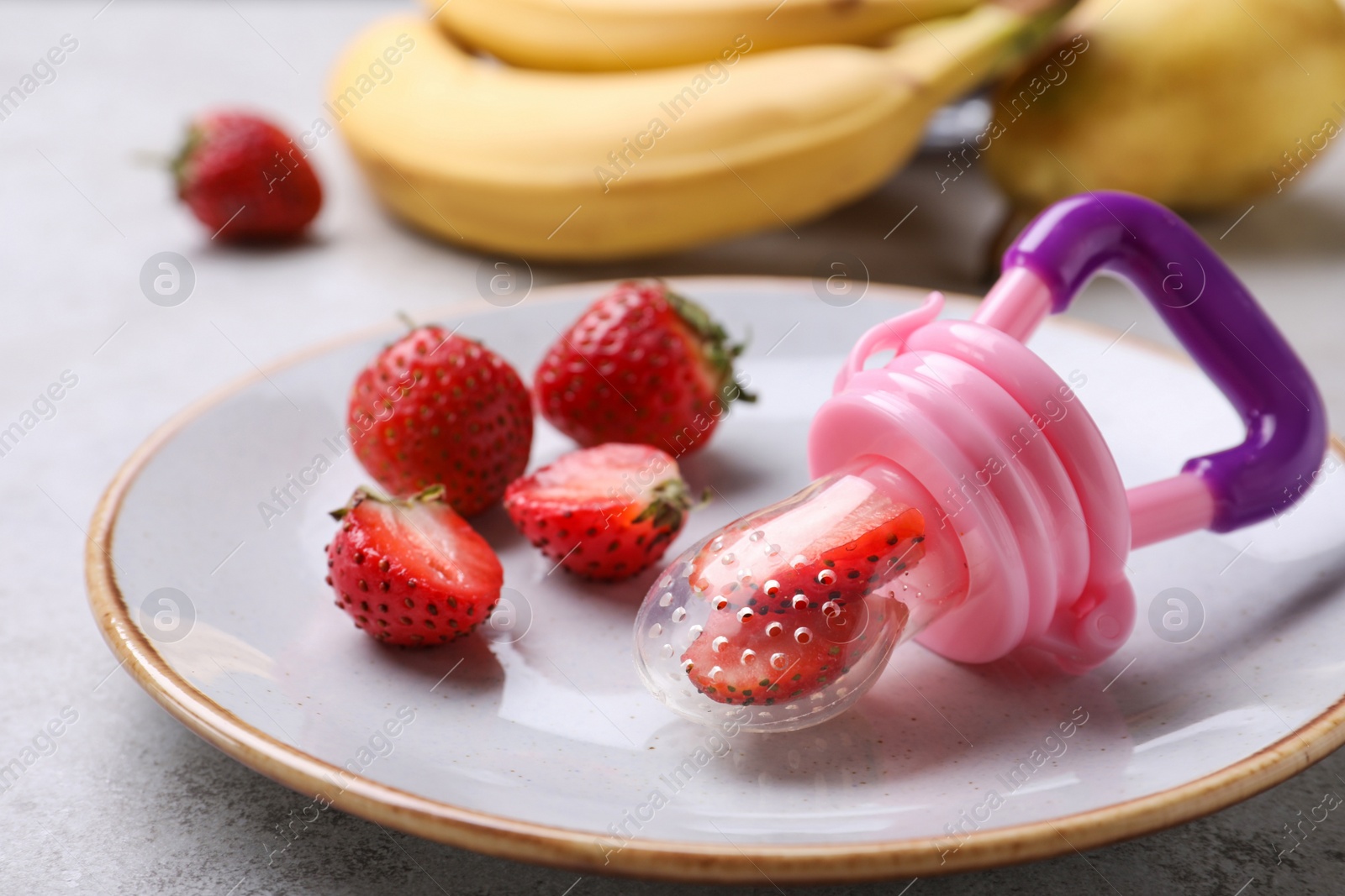 Photo of Plastic nibbler with fresh strawberries on light table, closeup. Baby feeder