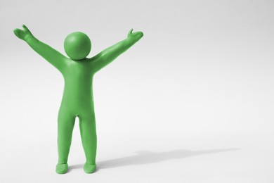 Photo of Human figure with arms wide open made of green plasticine on white background. Space for text