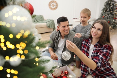 Happy family with cute child decorating Christmas tree together at home