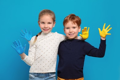 Photo of Little girl and boy with hands painted in Ukrainian flag colors on light blue background. Love Ukraine concept