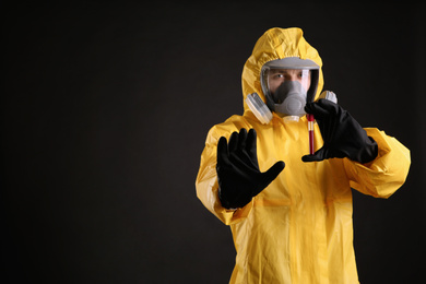 Photo of Man in chemical protective suit holding test tube of blood sample on black background, space for text. Virus research