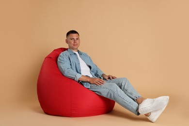 Photo of Handsome man on red bean bag chair against beige background