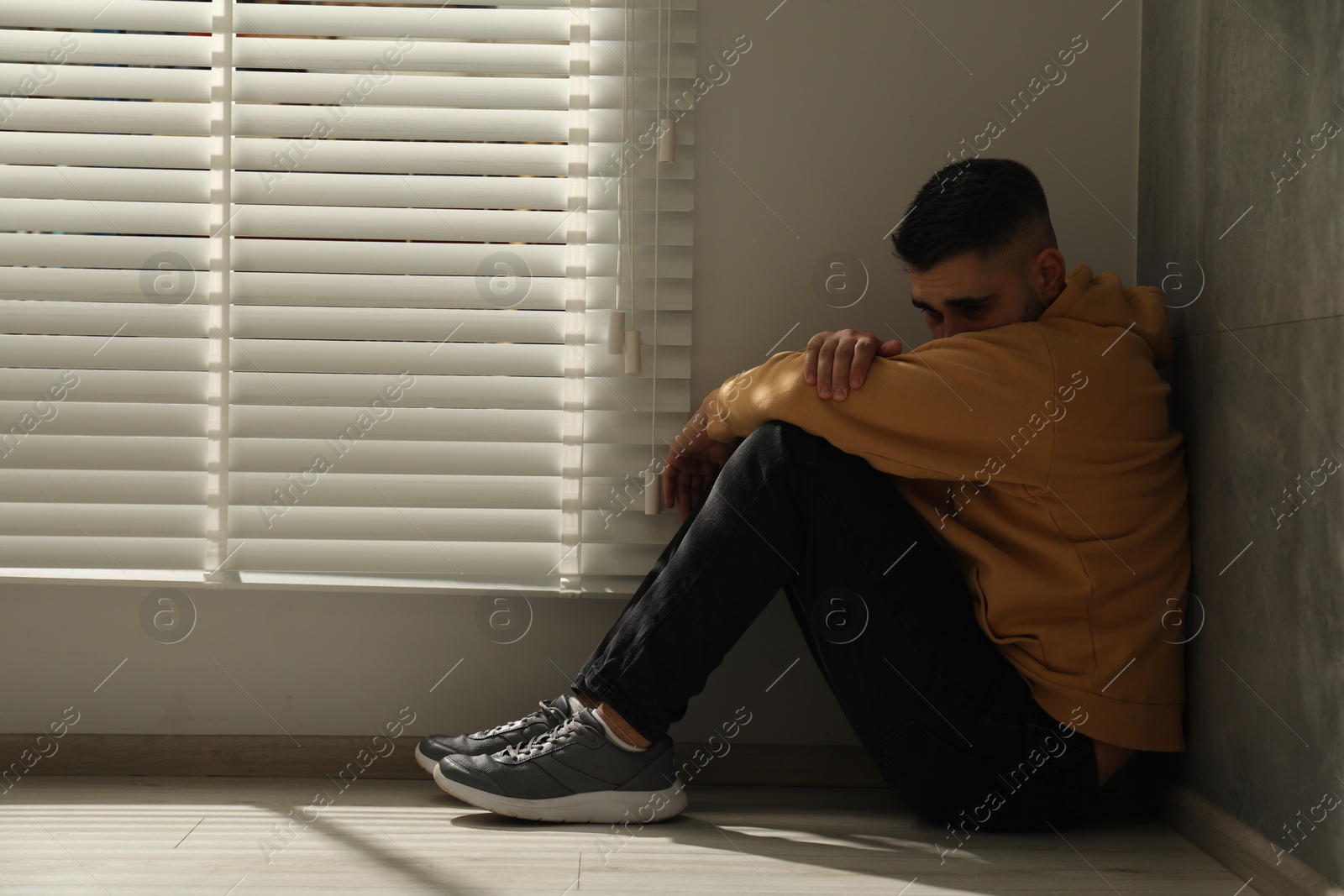 Photo of Sad man sitting on floor near window. Space for text