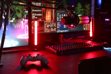 Photo of Playing video games. Modern computer, microphone and wireless controller on table indoors