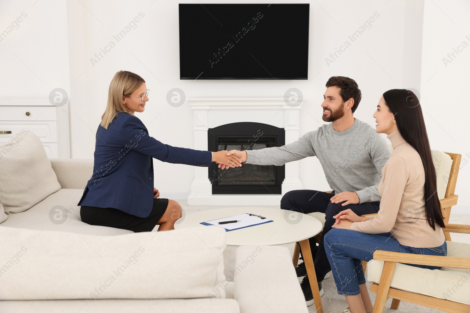 Photo of Real estate agent shaking hands with client at table in new apartment