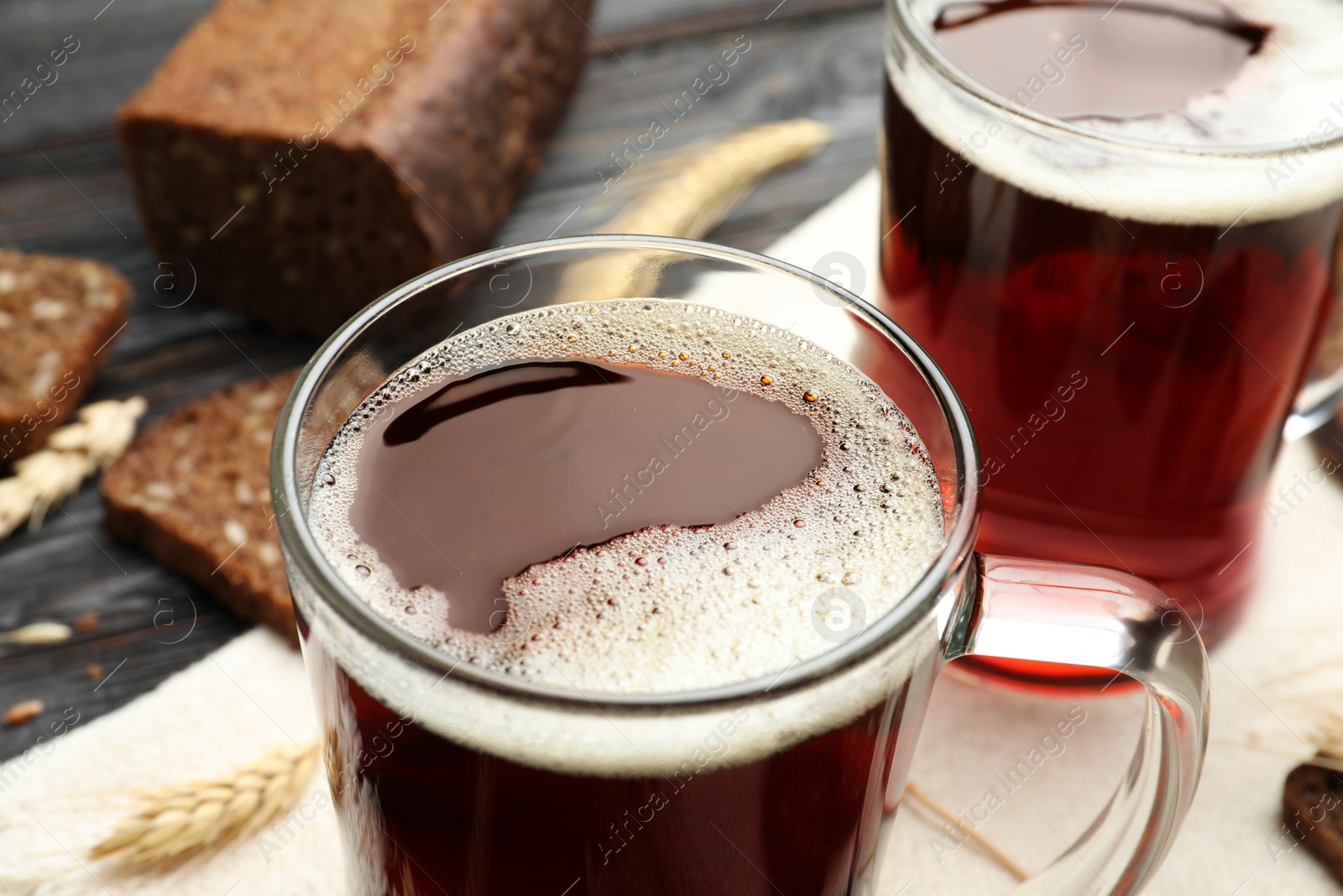 Photo of Mugs of delicious kvass, spikes and bread on table