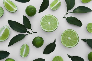 Photo of Whole and cut fresh limes with leaves on white background, flat lay