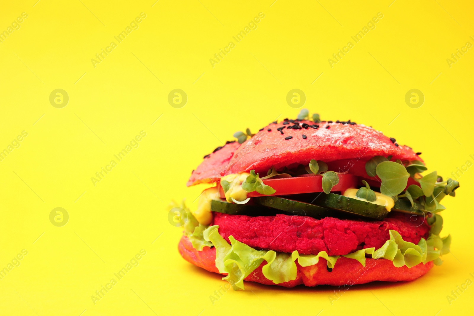 Photo of Tasty pink vegan burger with vegetables, patty and microgreens on yellow background, closeup. Space for text