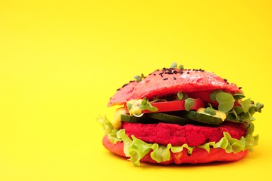 Tasty pink vegan burger with vegetables, patty and microgreens on yellow background, closeup. Space for text