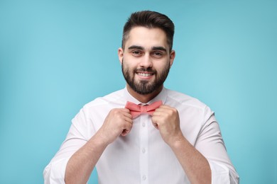 Photo of Smiling man in shirt adjusting bow tie on light blue background