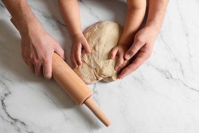 Father and child making dough at white table, top view