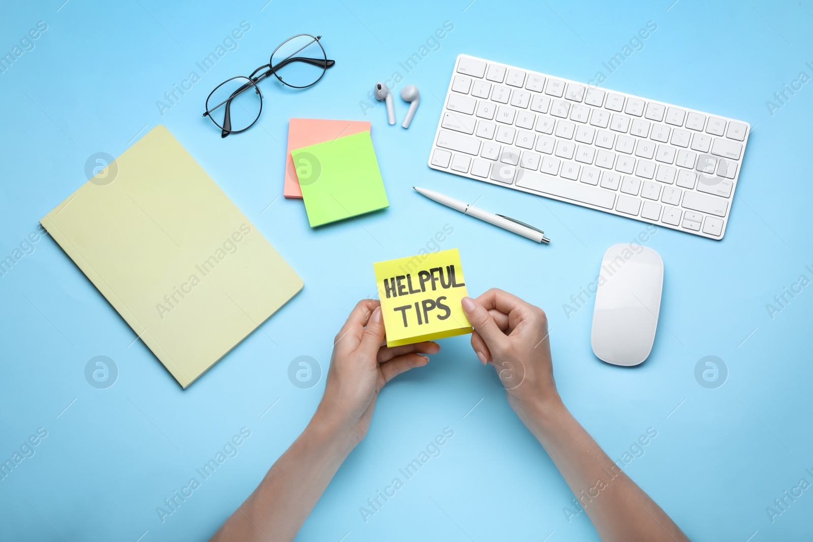 Photo of Woman holding paper note with phrase Helpful Tips at light blue table, top view
