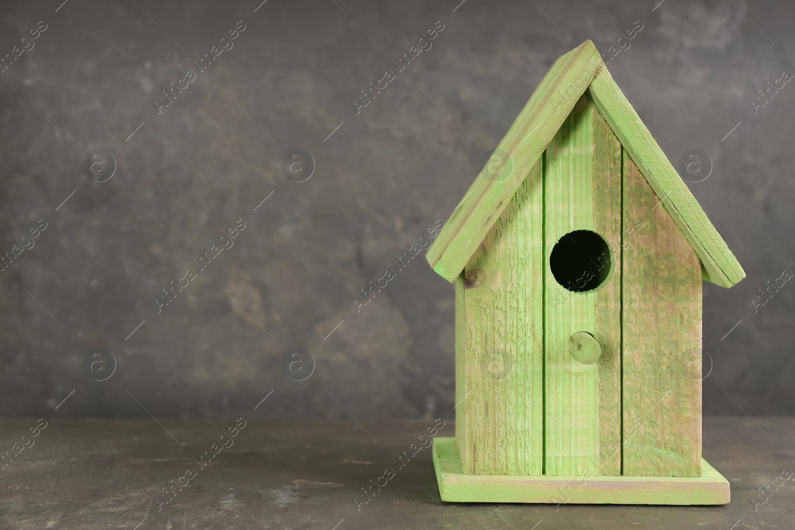 Photo of Beautiful bird house on grey stone table, space for text