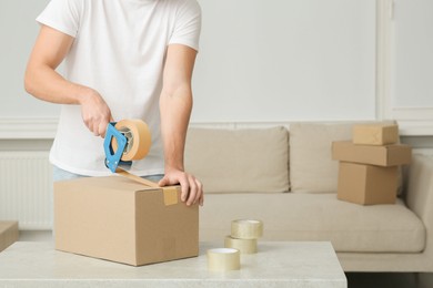 Photo of Man packing box with adhesive tape indoors, closeup