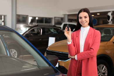 Young saleswoman with key near car in dealership