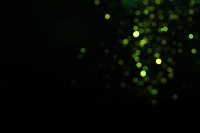 Blurred view of green lights on black background, space for text. Bokeh effect