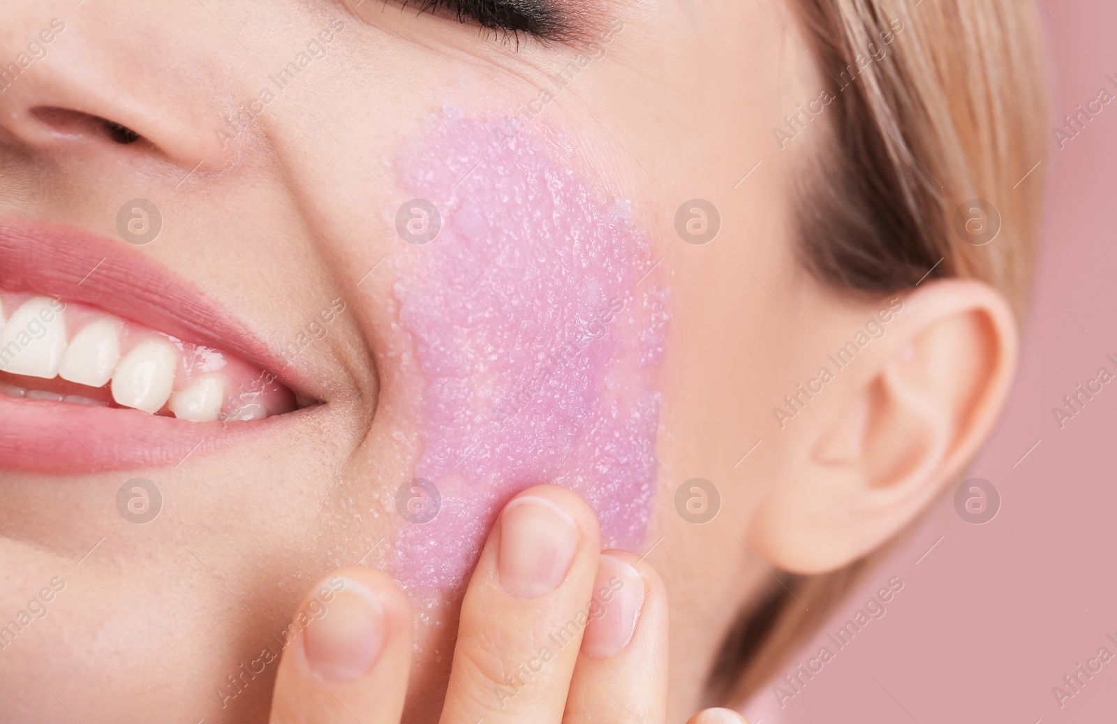 Photo of Young woman applying natural scrub on her face against color background, closeup