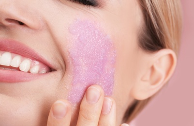 Young woman applying natural scrub on her face against color background, closeup