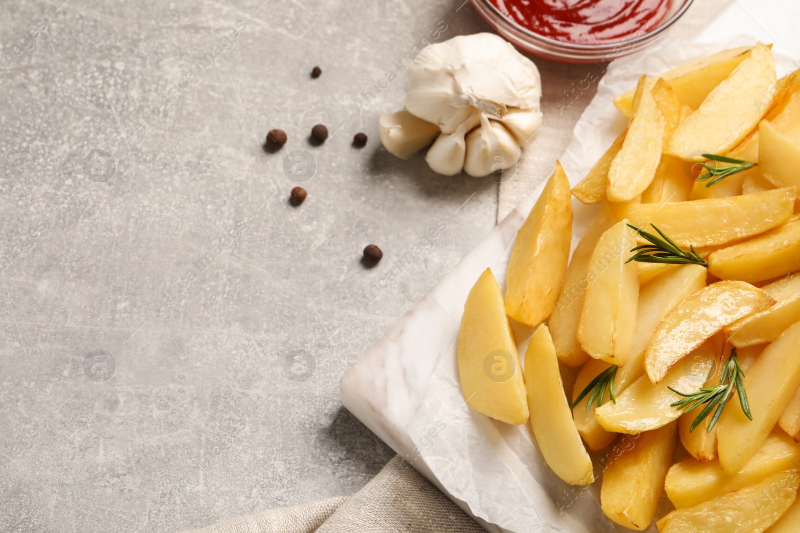 Photo of Tasty baked potato wedges, rosemary, garlic and sauce on grey table, flat lay. Space for text