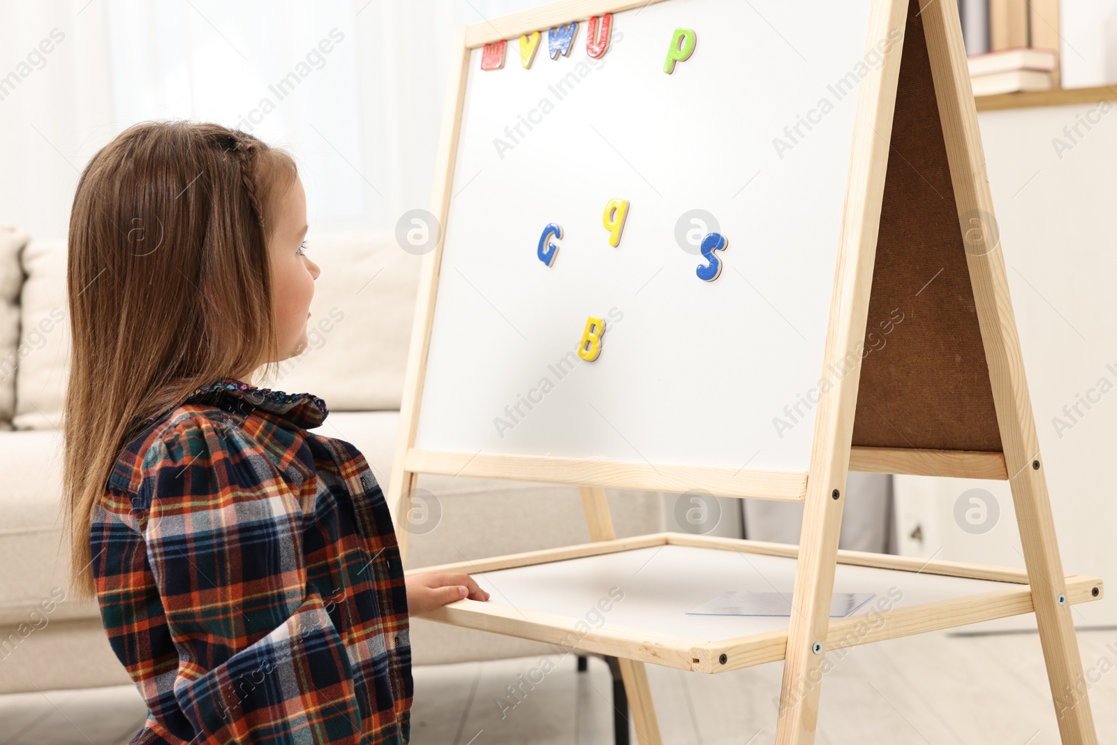 Photo of Cute little girl putting magnetic letters on board at home. Learning alphabet