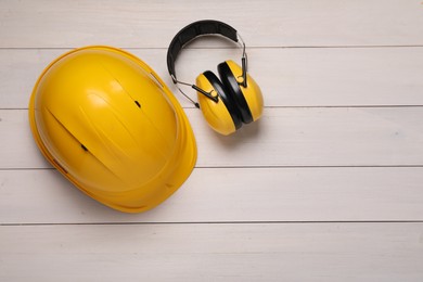 Photo of Hard hat and earmuffs on white wooden table, flat lay with space for text. Safety equipment