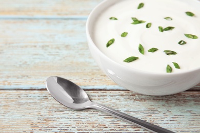 Photo of Bowl of fresh sour cream with green onion and spoon on light blue wooden table. Space for text