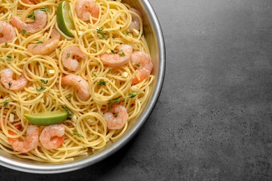 Frying pan with spaghetti and shrimps on grey background, top view