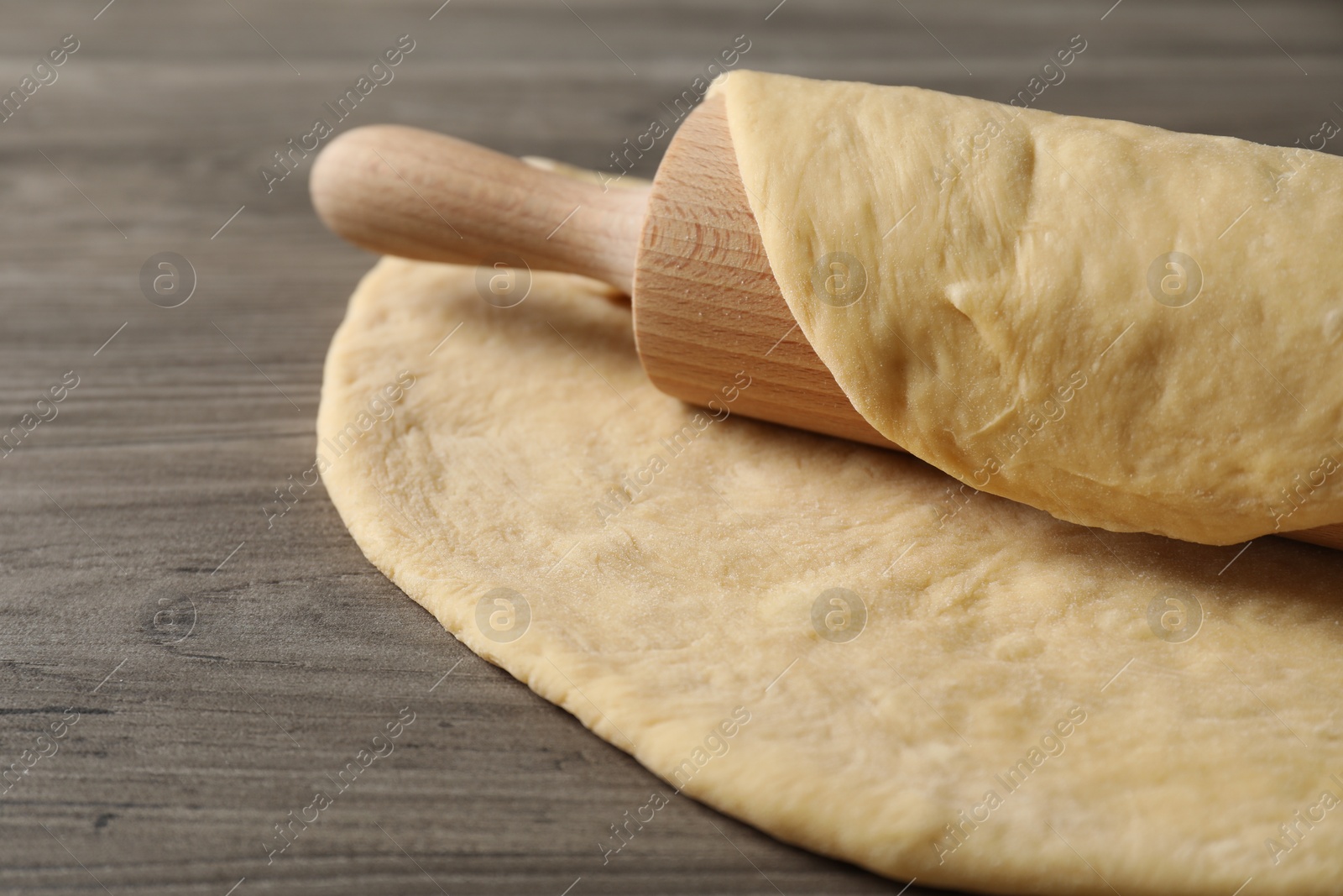 Photo of Raw dough and rolling pin on wooden table, closeup