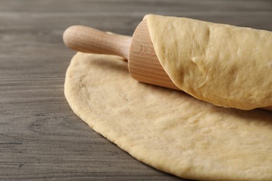 Photo of Raw dough and rolling pin on wooden table, closeup