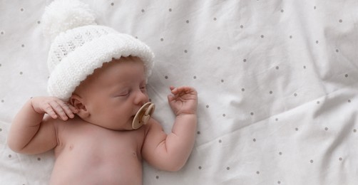 Cute newborn baby in white knitted hat sleeping on bed, top view with space for text. Banner design
