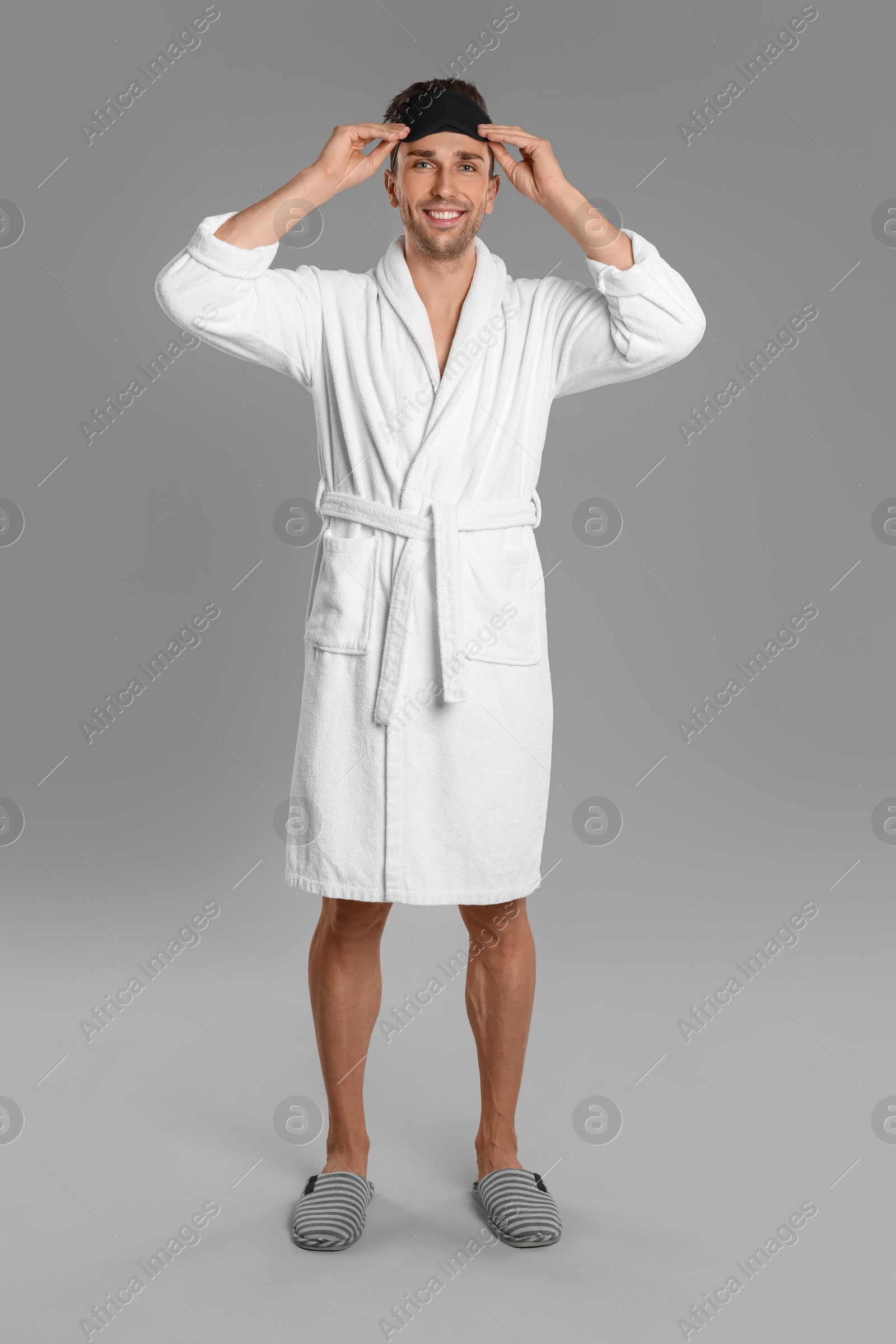 Photo of Happy young man in bathrobe on grey background