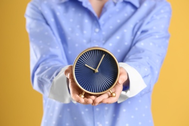 Young woman holding alarm clock on color background. Time concept