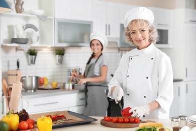 Photo of Professional female chef cutting pepper on table in kitchen