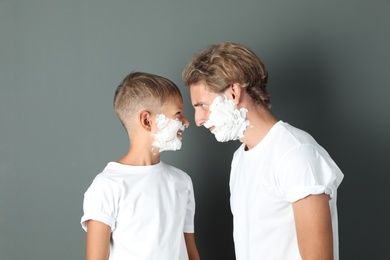 Father and son with shaving foam on faces against color background