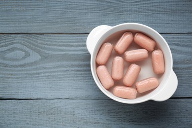 Bowl of delicious sausages on grey wooden table, top view. Space for text