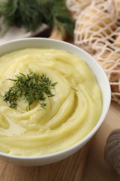 Photo of Bowl of tasty cream soup with dill on wooden table, closeup